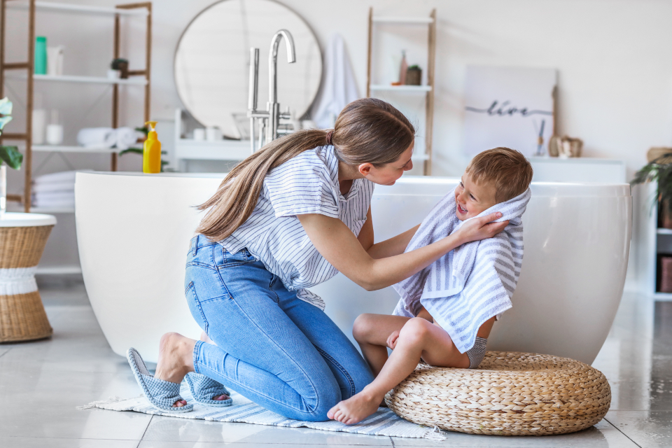 A mother drying her son with a towel in a bright bathroom