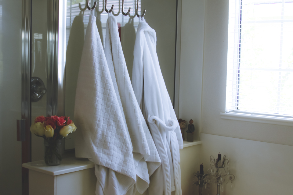 White towels and a robe hanging on hooks in a bathroom