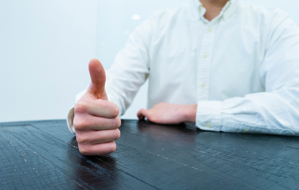 A hand giving a thumbs up gesture at a dark wooden table