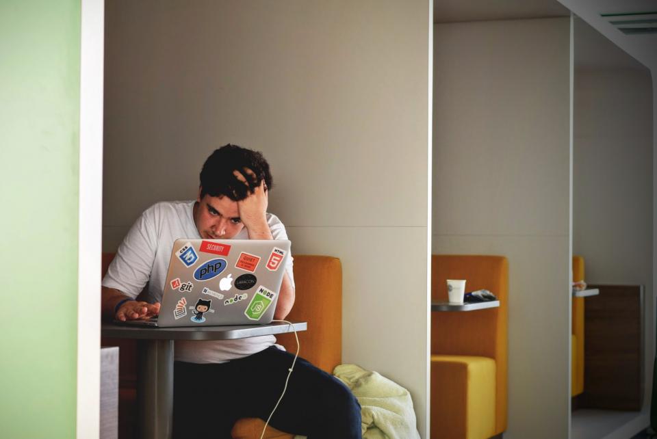 A stressed person resting their head on their hand at a laptop