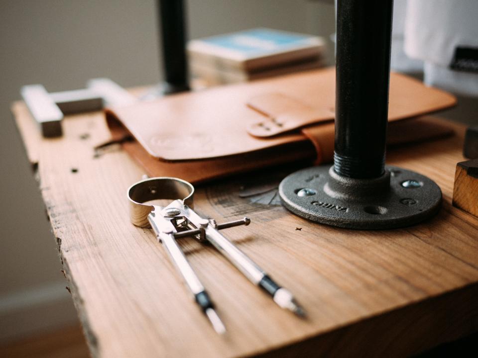 A drafting compass resting on a wooden workbench
