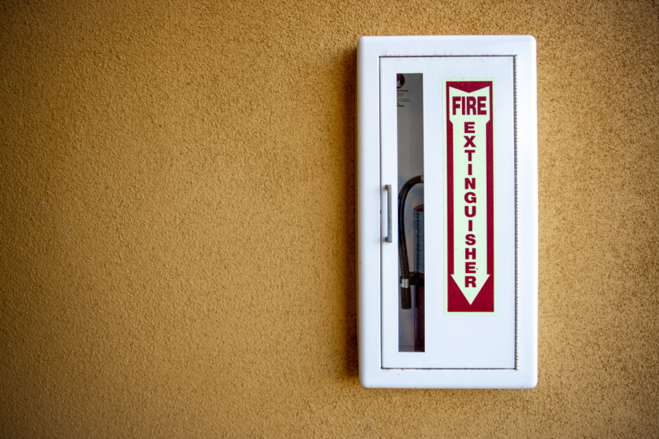 A fire extinguisher mounted in a case on an orange wall