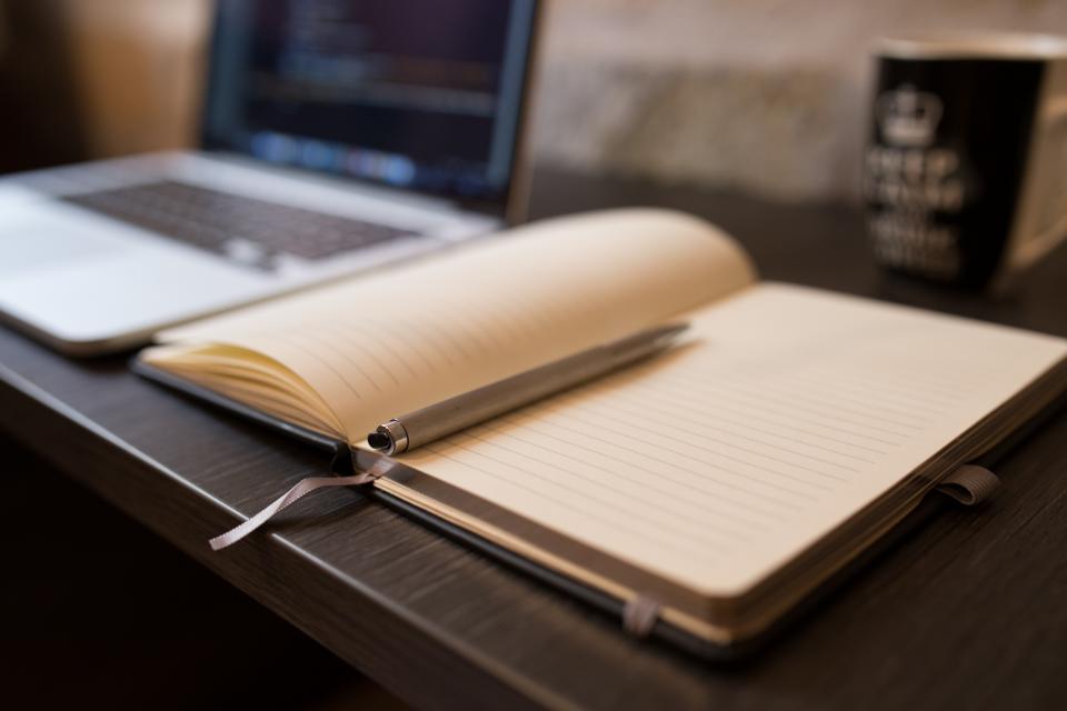 An open notebook and pen on a desk next to a laptop