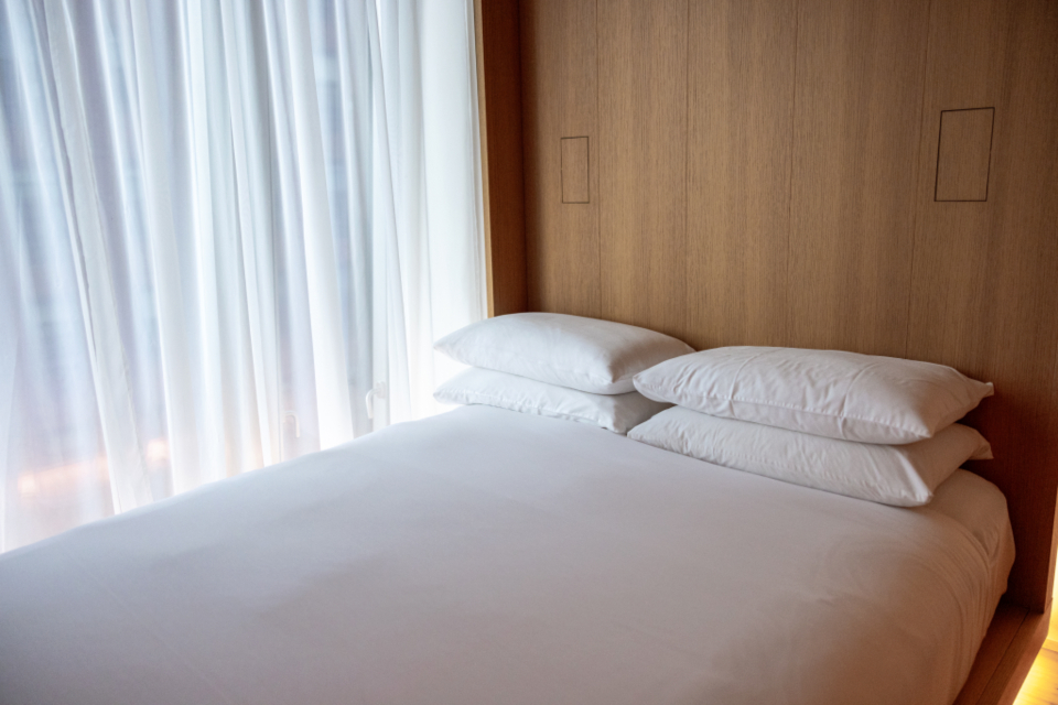 A freshly made hotel bed with white pillows and sheer curtains