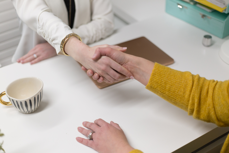 Two people shaking hands over a desk with a coffee cup