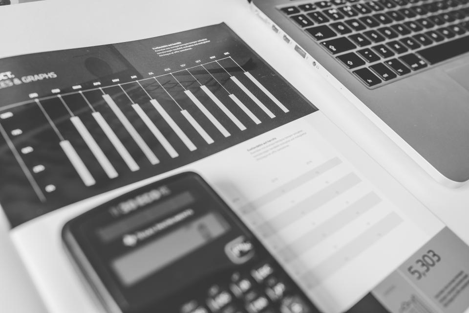 A calculator resting on a printed financial chart next to a laptop