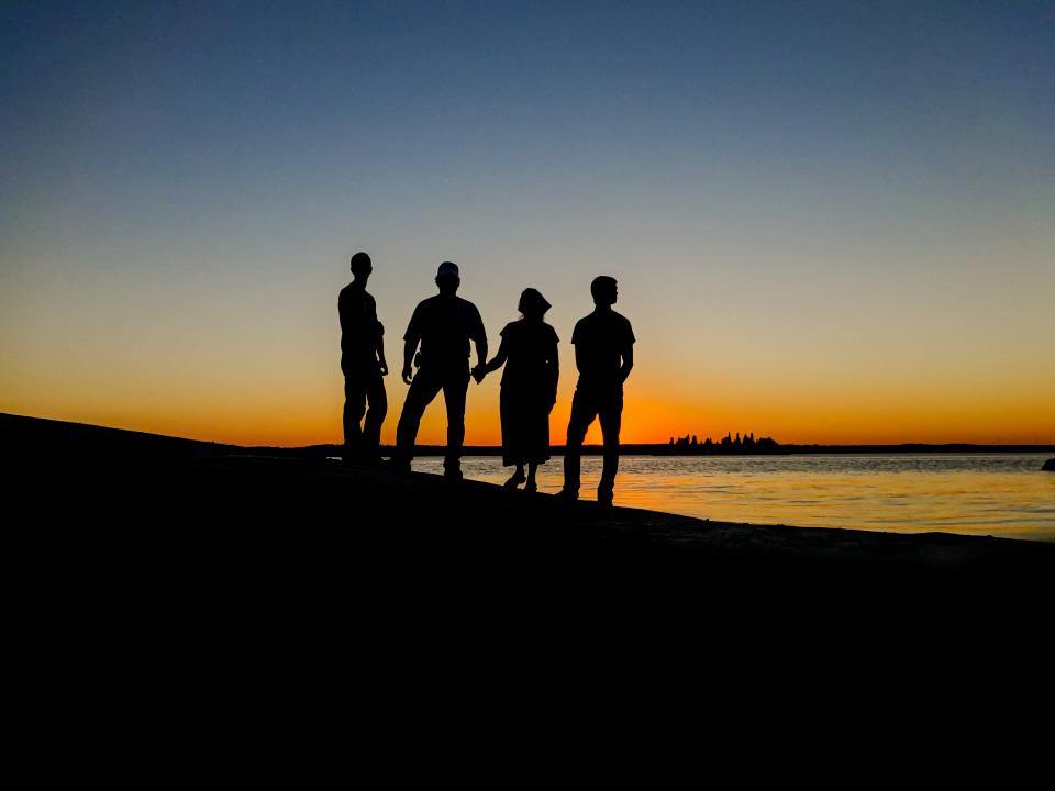 A family silhouette standing together at sunset by water