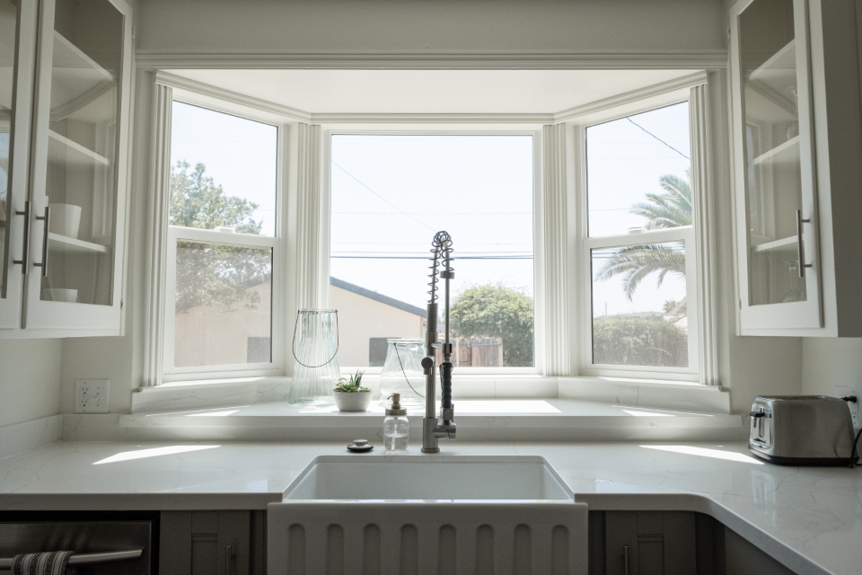 A farmhouse kitchen window above a sink looking out to trees