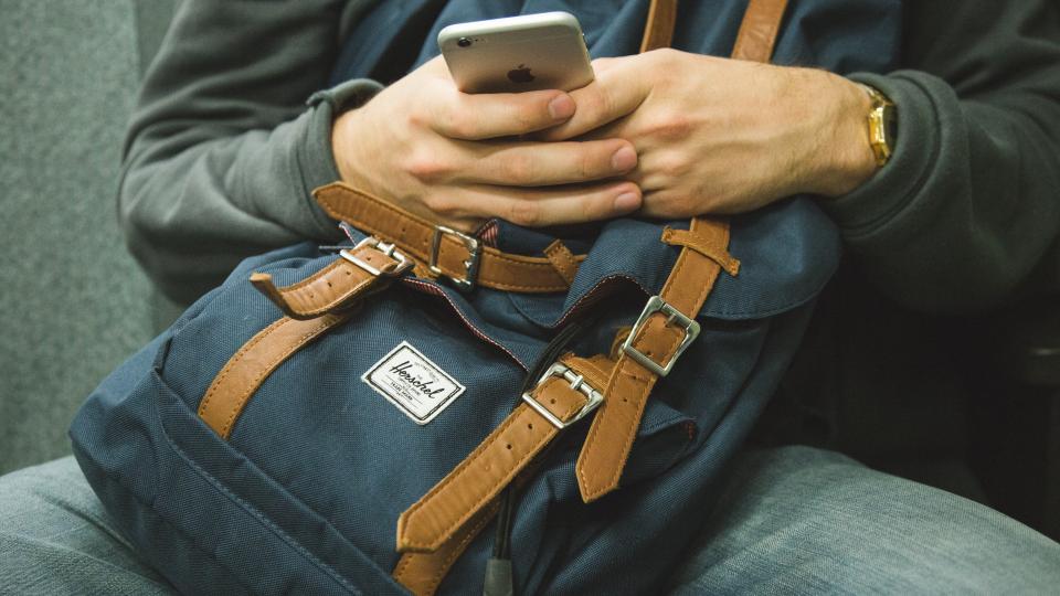 A traveler holding a phone while resting a hand on a packed backpack
