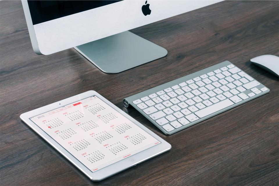 A tablet showing a calendar app next to a keyboard and desktop computer